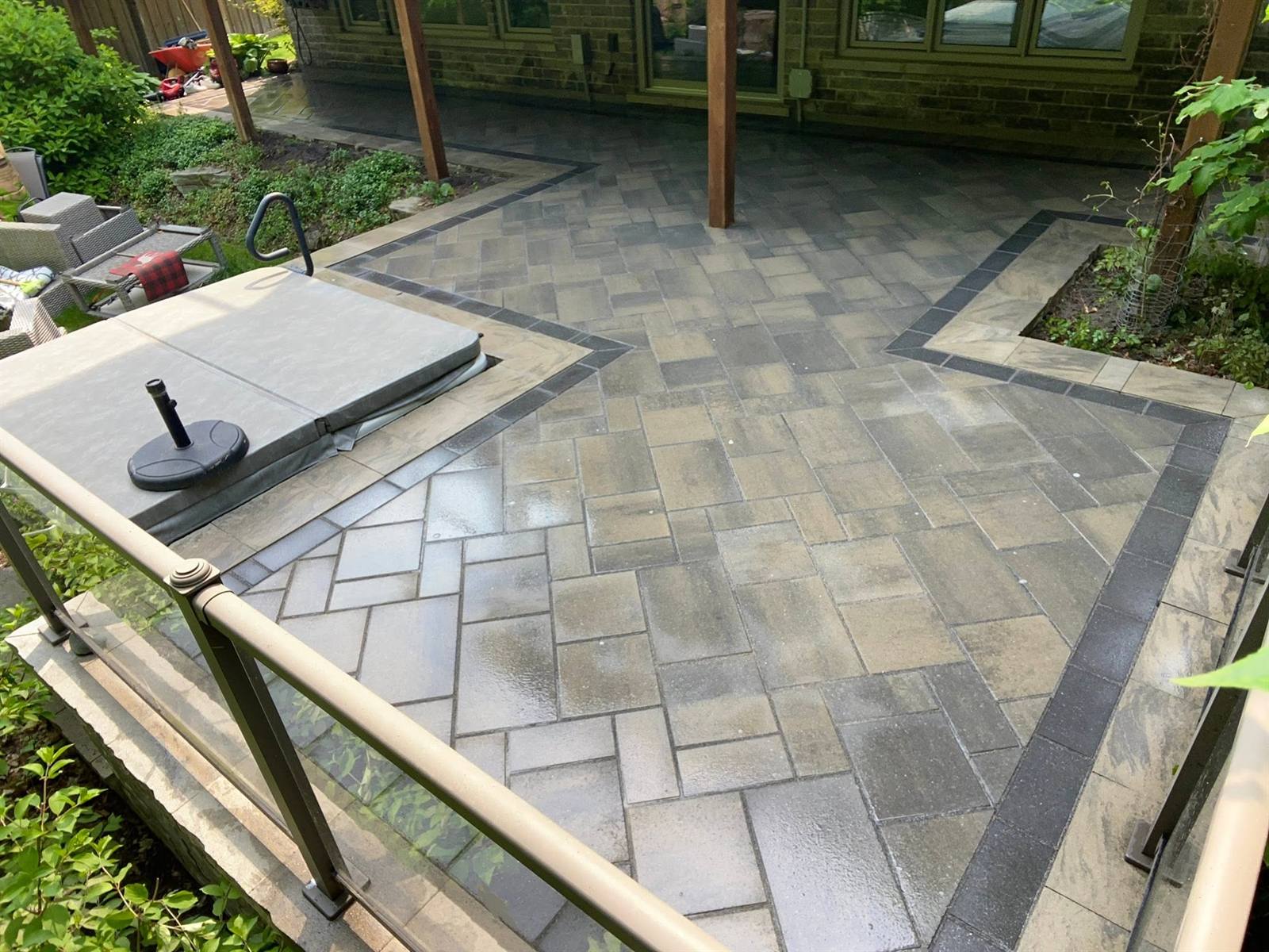 Interlock patio with banded border and glass railing around a hot tub in Kingston, Ontario