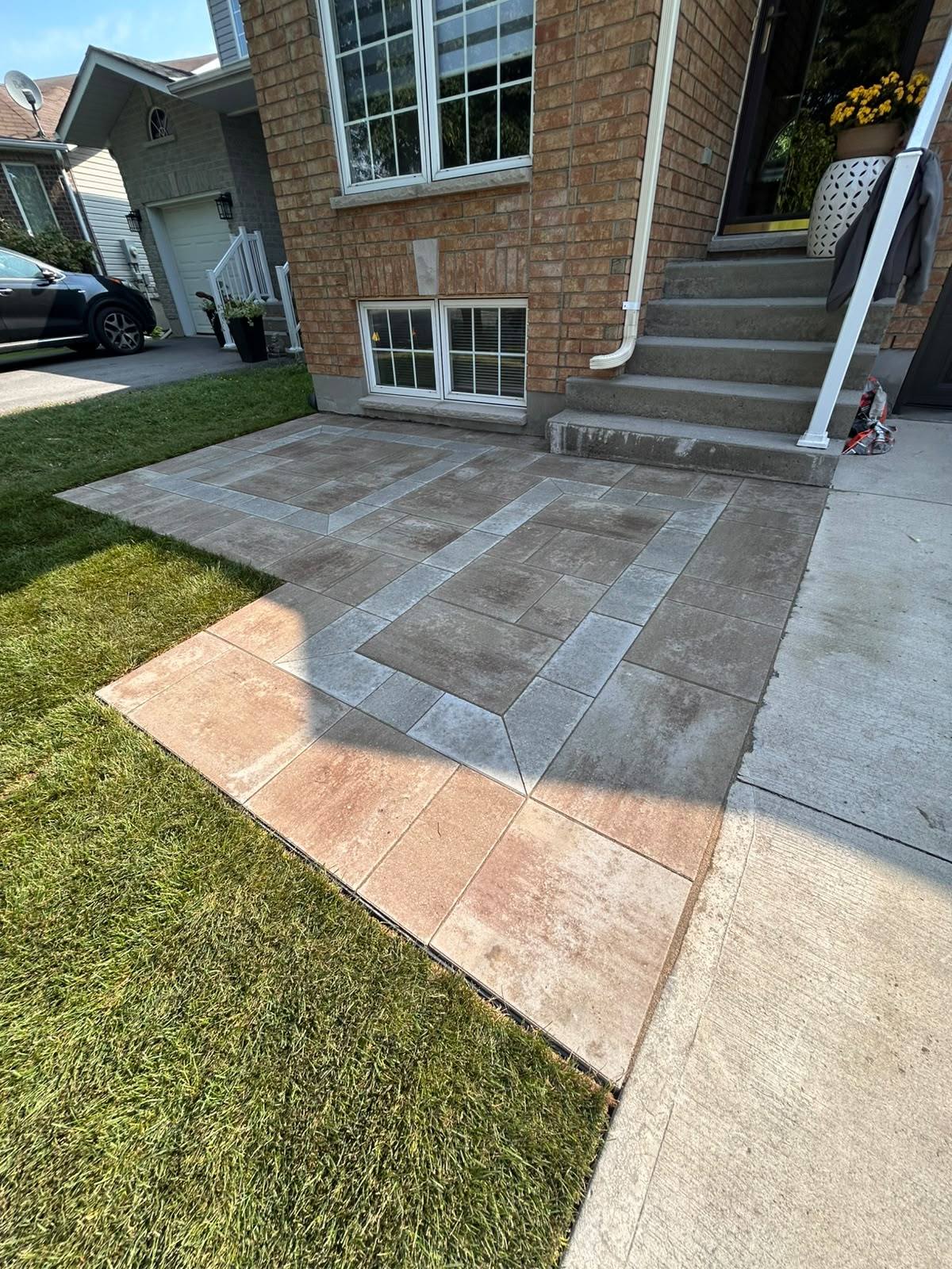 Interlock walkway with a grey field, contrasting tan border and geometric inlay leading to a front entrance in Kingston, Ontario